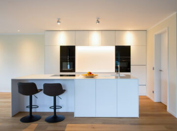 Moderne, weiße Küche mit Barhocken und Bolzbodenbelag