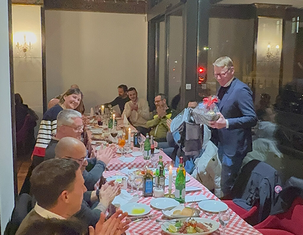 Weihnachtsfeier Ewering Berlin Mitarbeiter Tischtafel Weihnachtsfeier von der Ewering Berlin GmbH. Ewering Mitarbeiter sitzen in einem Lokal an einer gedeckten Tischtafel und übergeben ein Geschenk an den Chef.