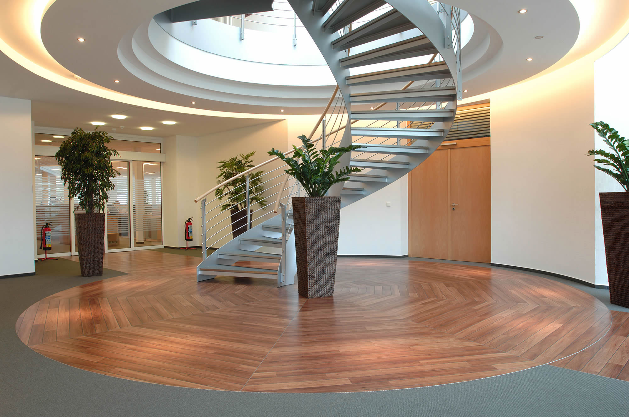 Modernes Treppenfoyer mit rundem Grundriss und hochwertig verlegtem Amtico Designboden in Holzoptik. Das Bild zeigt sauber ausgeführte Bodenbelagsarbeiten in einem repräsentativen Eingangsbereich.