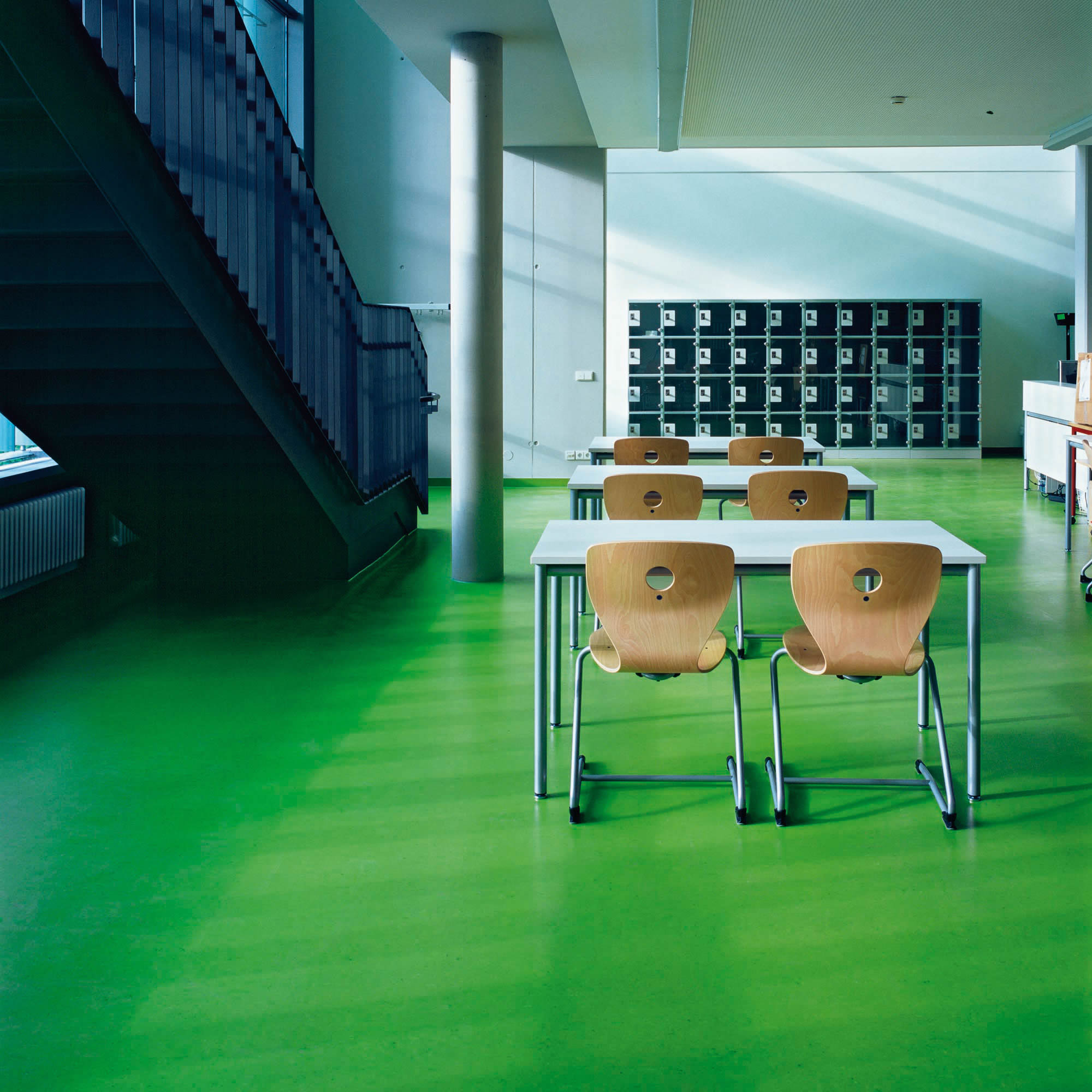 Moderner Lern- und Aufenthaltsbereich mit grünem Linoleumboden, Tischen und Stühlen. Das Bild zeigt sauber ausgeführte Bodenbelagsarbeiten in einem stark genutzten Objektbereich mit robuster und gepflegter Raumwirkung.