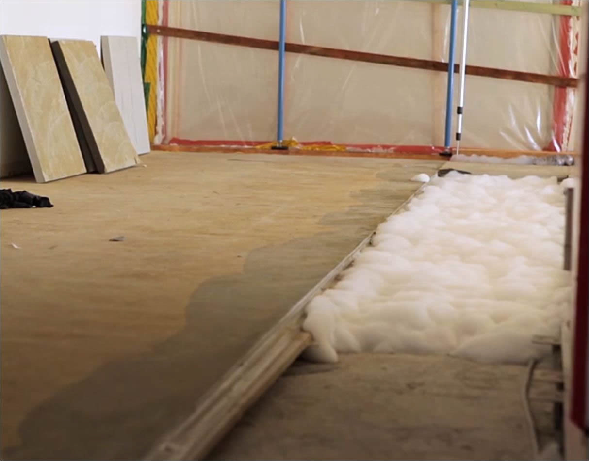 Geöffneter Bodenaufbau mit freigelegter Dämmschicht neben einer angehobenen Bodenplatte nach einem Wasserschaden.