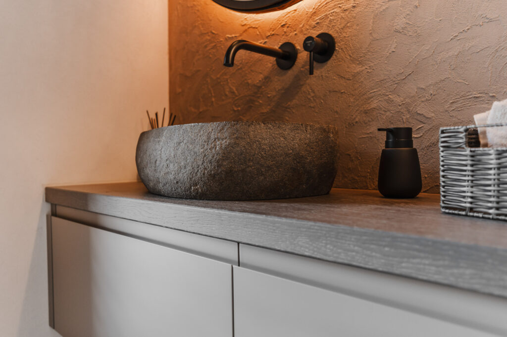 Detailaufnahme eines modernen Waschplatzes mit Frescolori Wandgestaltung, dunklem Steinbecken, schwarzer Armatur, Hängeleuchte und schwebendem Waschtisch.