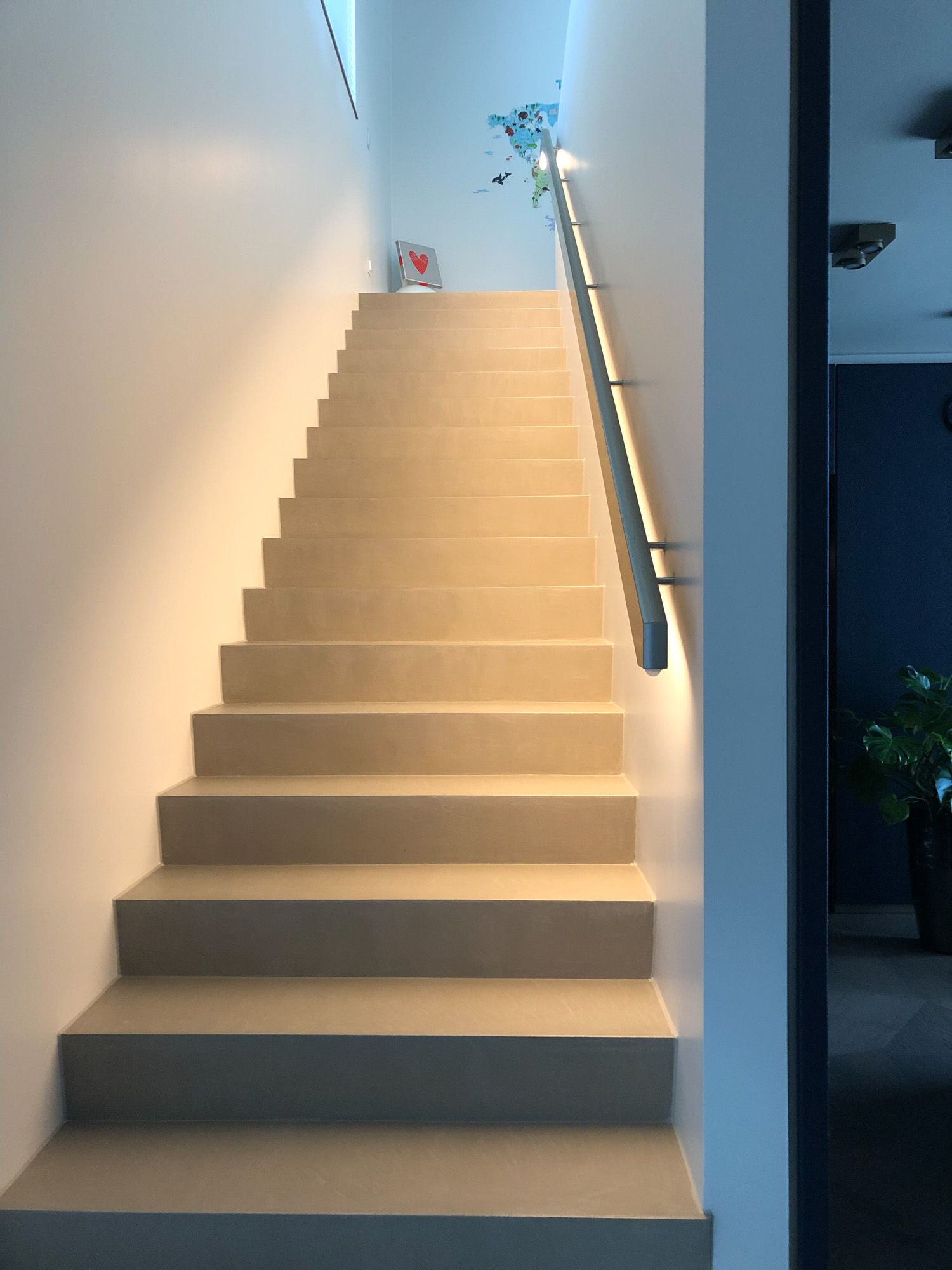 Modernes Treppenhaus mit hellen Frescolori Treppenstufen, weißen Wänden, beleuchtetem Handlauf und reduzierter, klarer Architektur.