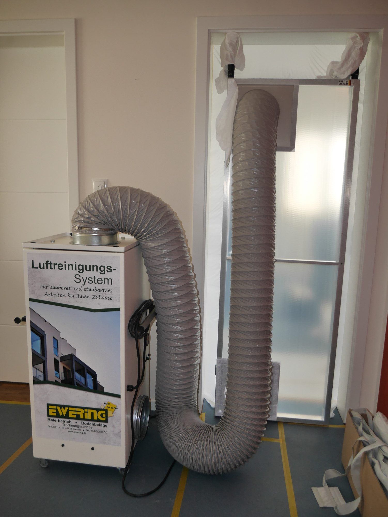 Mobiles Luftreinigungssystem mit großem Schlauch an einer abgedichteten Türöffnung für sauberes und staubarmes Arbeiten im Innenbereich.