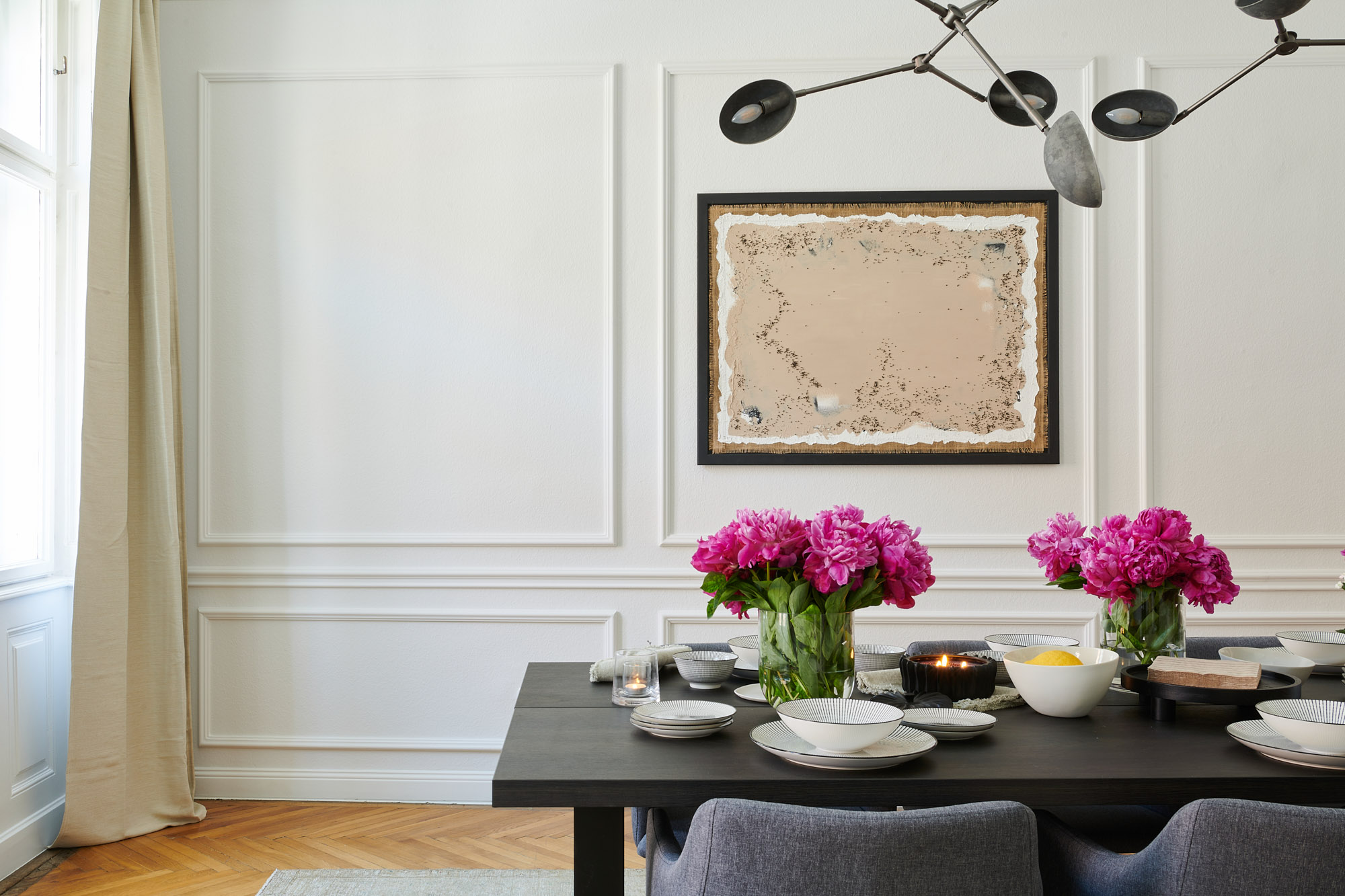 Stilvolles Esszimmer mit weißen Stuckleisten und Wandleisten, schwarzem Esstisch, pinken Blumen, Wandbild und Fischgrätparkett.