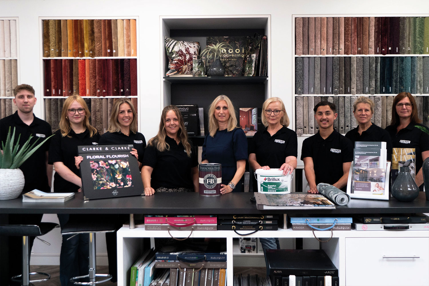 Das Team vom Ewering Fachmarkt steht vor den Teppichmustern und zeigt Produkte.