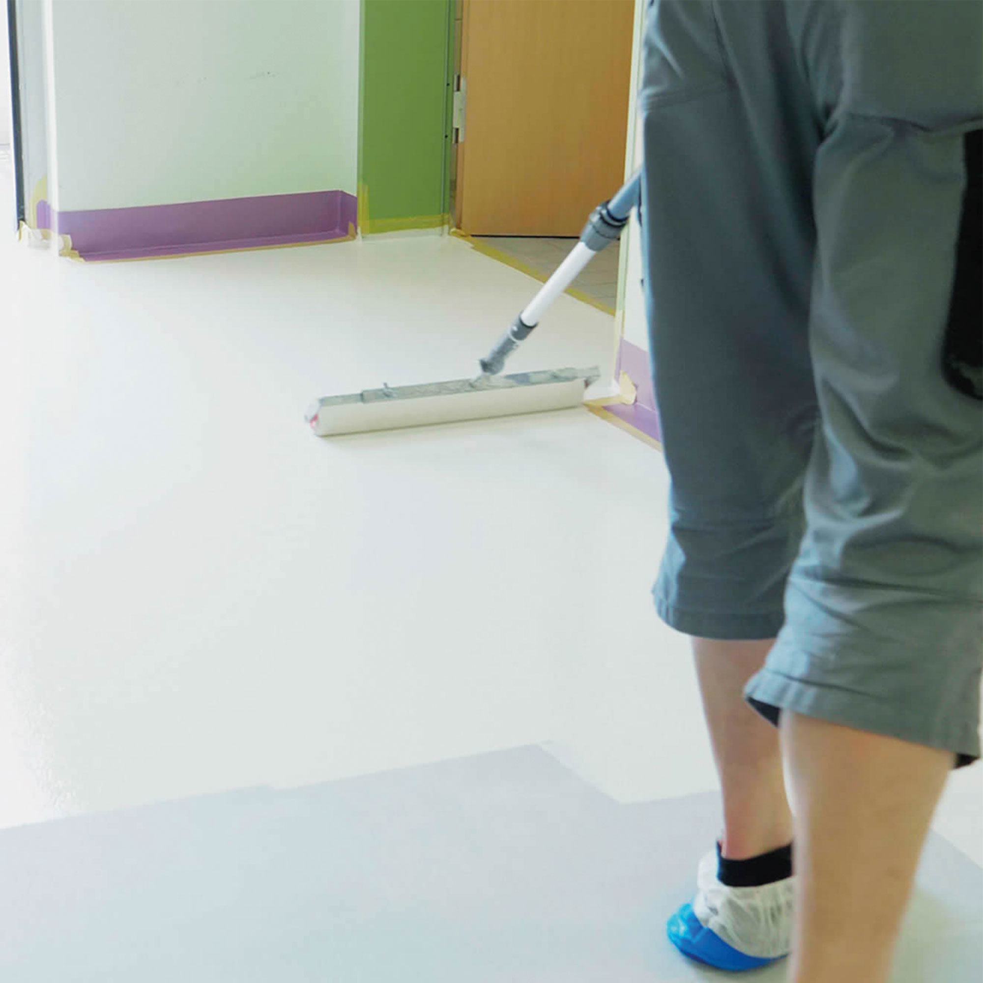 Mitarbeiter trägt mit einer Rolle eine neue Bodenbeschichtung auf einen hellen Boden auf.