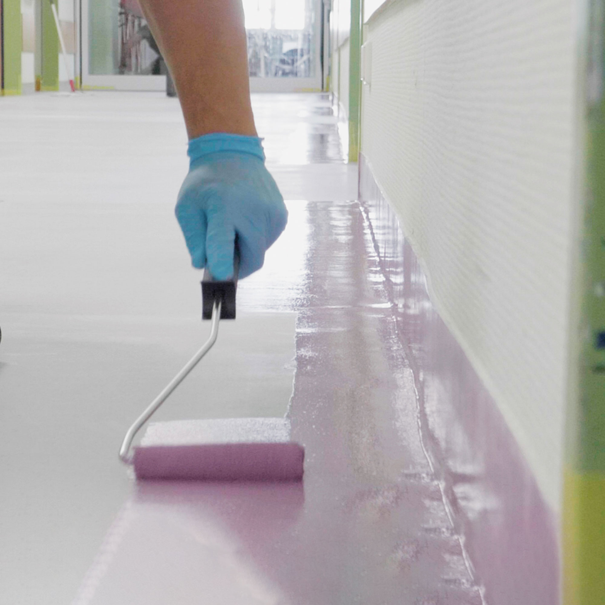 Hand mit Farbrolle beschichtet sorgfältig den Randbereich eines Bodens.