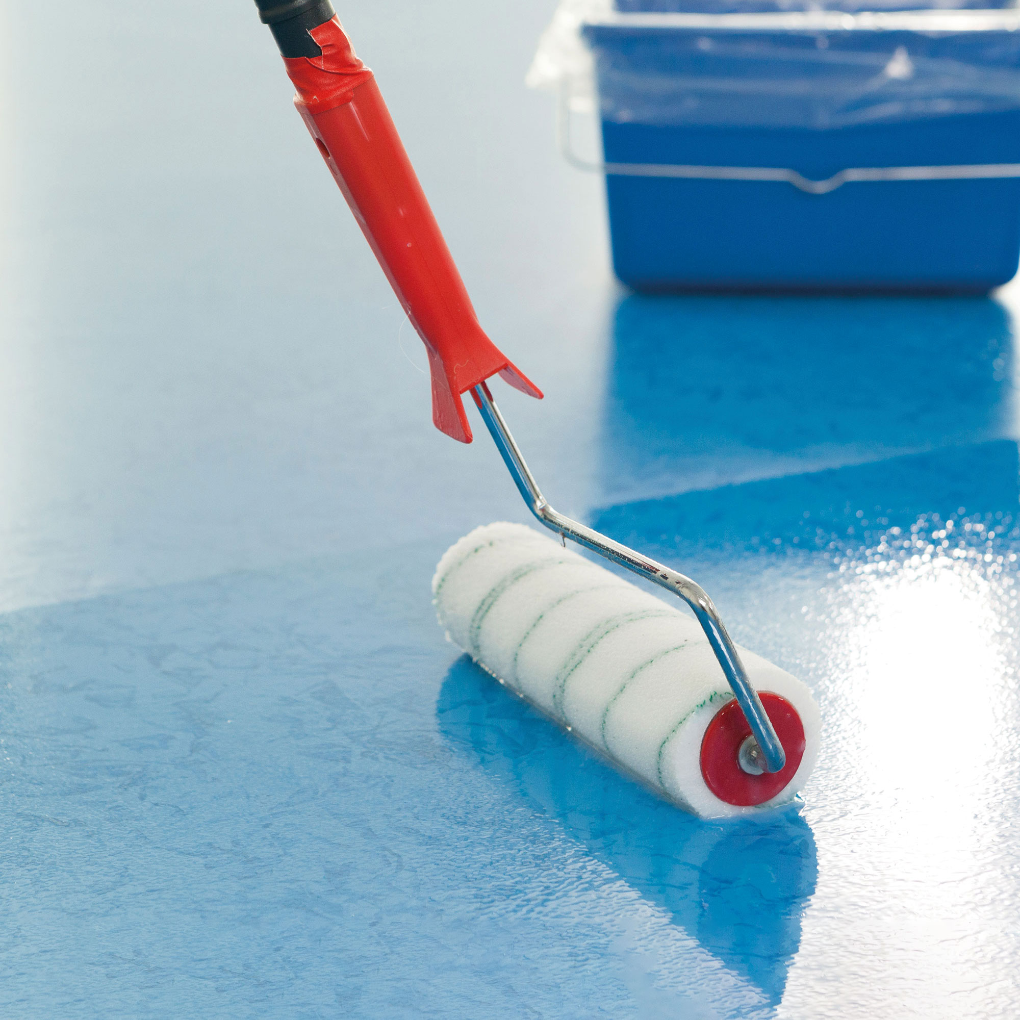 Farbrolle trägt eine Versiegelung auf einen blau beschichteten Boden auf.