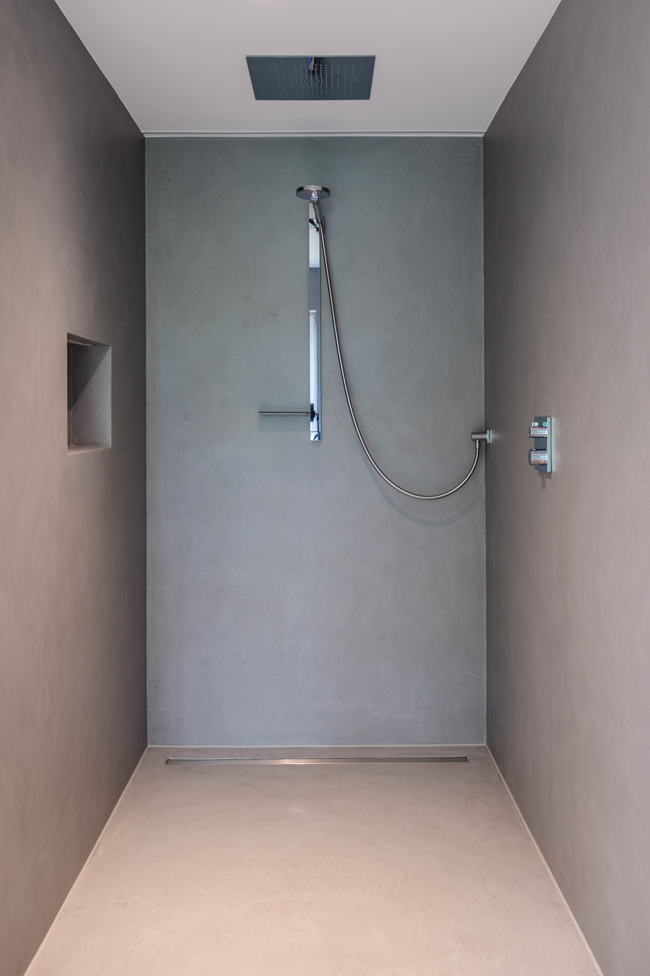 Fugenlose Dusche mit grauen, nahtlosen Wandflächen und modernem Duschsystem