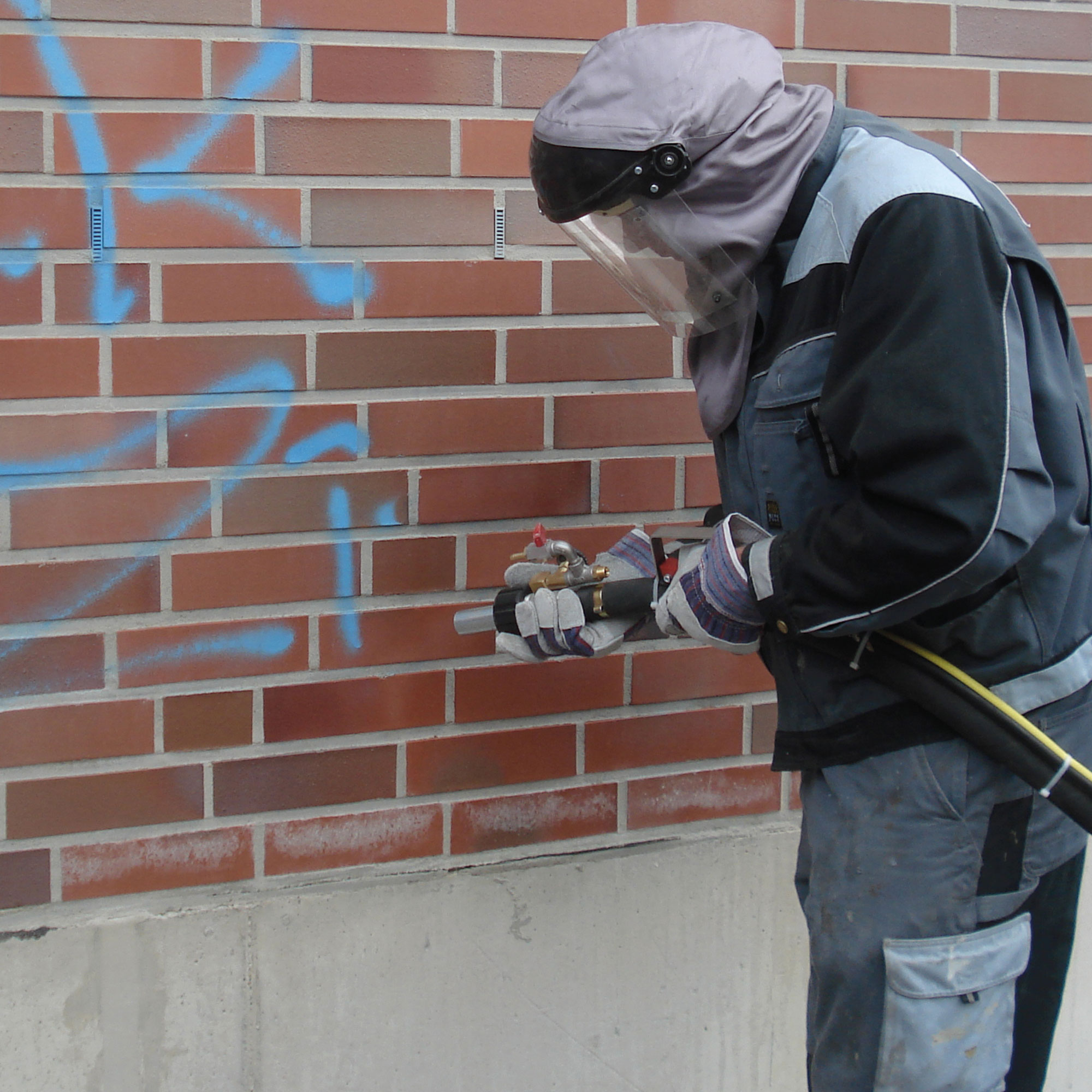 Mitarbeiter entfernt Graffiti mit spezieller Strahltechnik von einer Klinkerfassade.