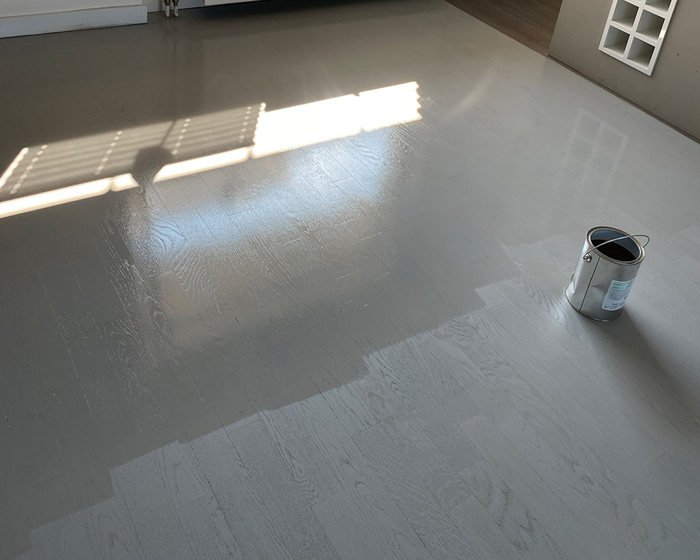 Heller Parkettboden mit frischer Lasur während der Endbehandlung, daneben steht ein Metalleimer.